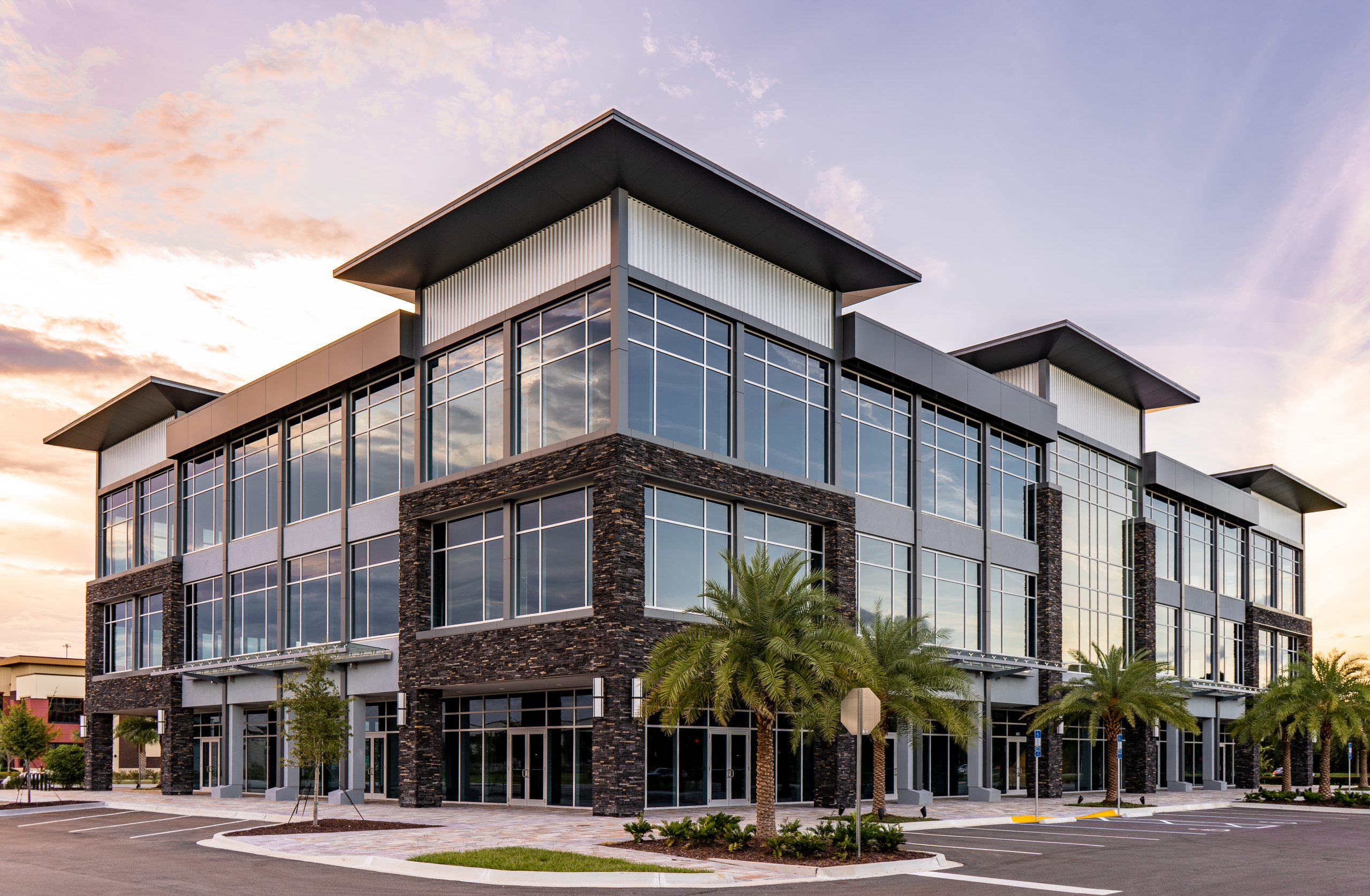 An external view of a three-story office building with large glass windows surrounded by palm trees.